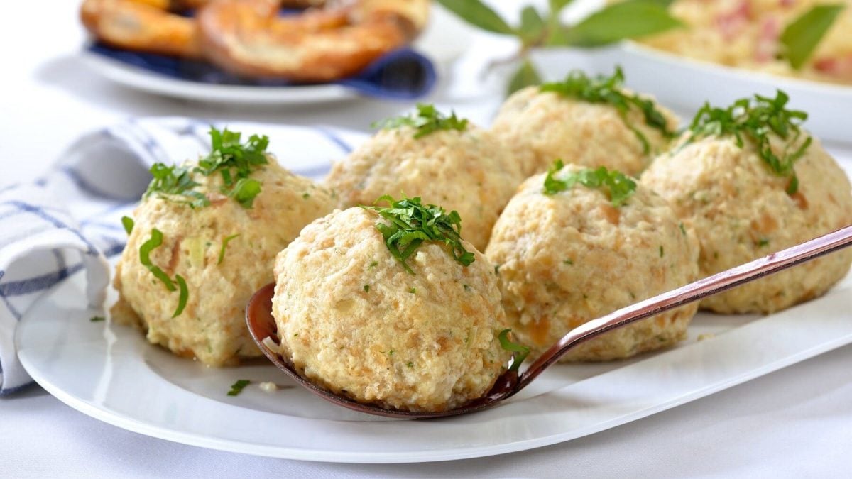 Bayerische Semmelknödel mit Petersilie liegen auf einer weißen Servierplatte, dahinter liegen Brezeln auf einem Teller
