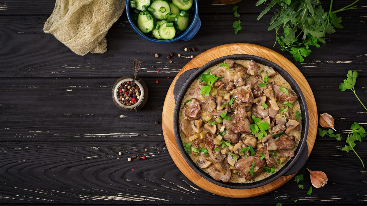 Boeuf Stroganoff auf schwarzem Holz. Kräuter und Stofftuch auf dem Tisch. Aufnahme aus der Vogelperspektive.