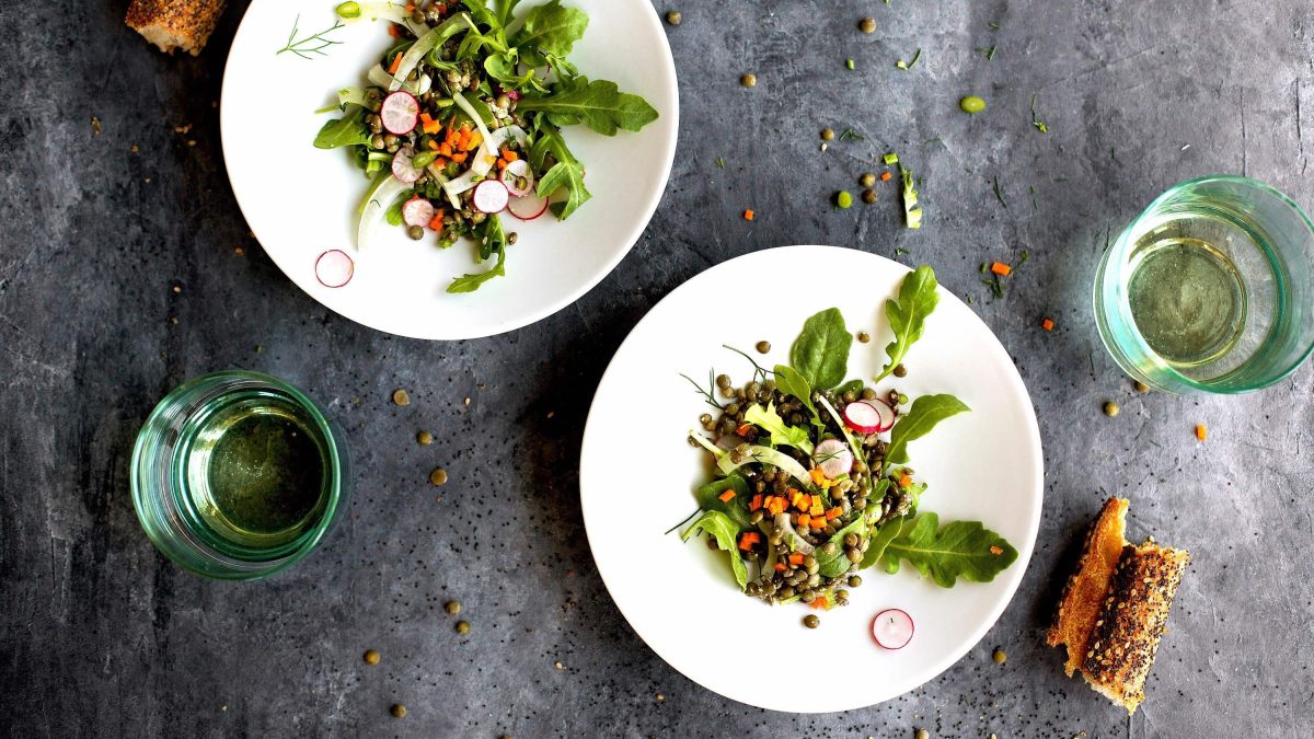 Linsensalat mit Rucola, frischen Radieschen, Möhrenstückchen und Dill auf kleinen Tellern mit Sesamring serviert auf steinerner Unterlage