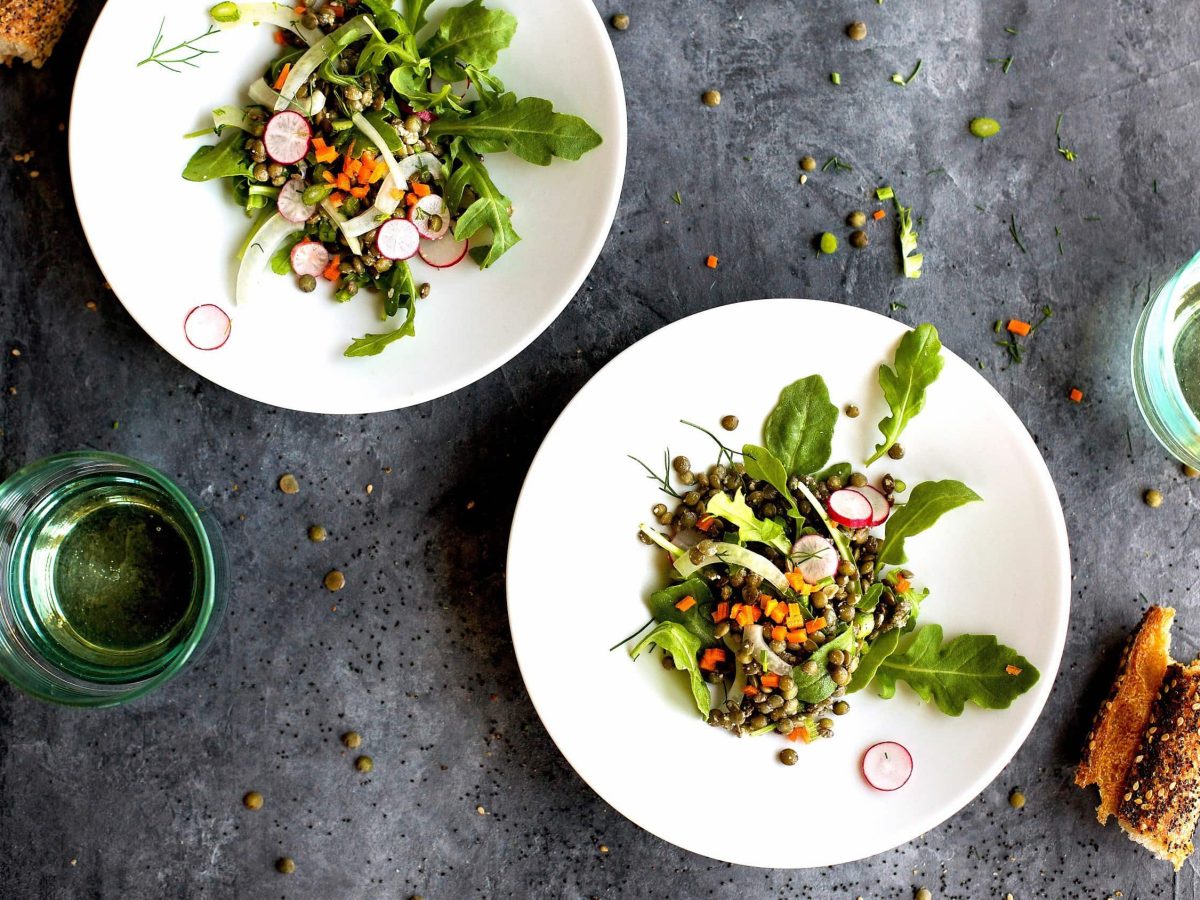 Linsensalat mit Rucola, frischen Radieschen, Möhrenstückchen und Dill auf kleinen Tellern mit Sesamring serviert auf steinerner Unterlage
