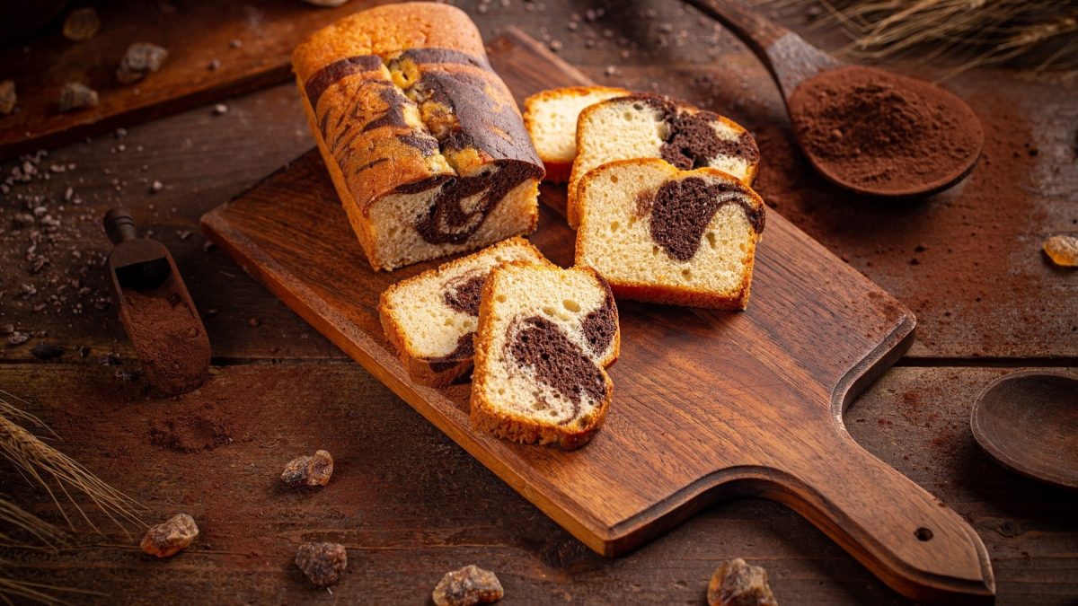 Klassischer Marmorkuchen aus der Kastenform, geschnitten und drapiert auf einem dunklen Holzbrett auf rustikalem Tisch.