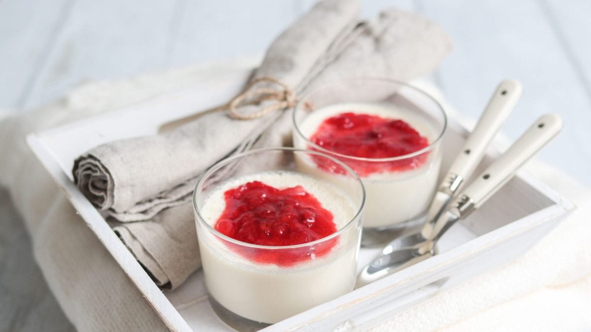 Panna Cotta mit selbst gemachter Erdbeersauce in zwei Gläsern auf weißem Tablett