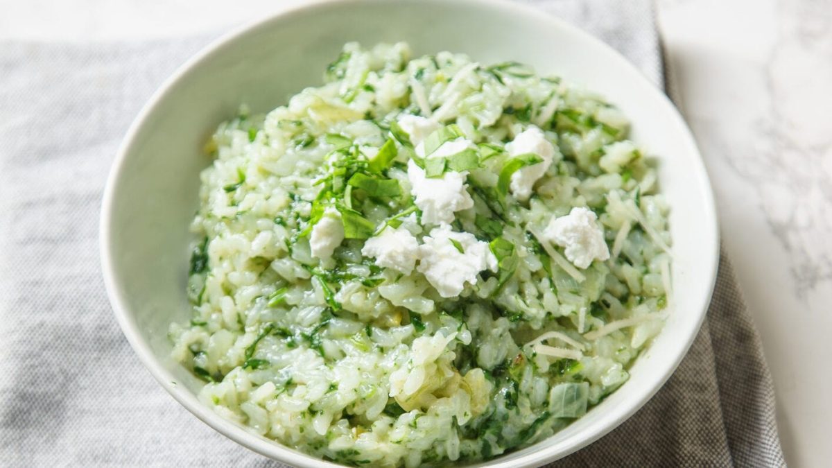 Spinat-Risotto mit Ziegenkäse auf weißem Teller vor marmoriertem Untergrund