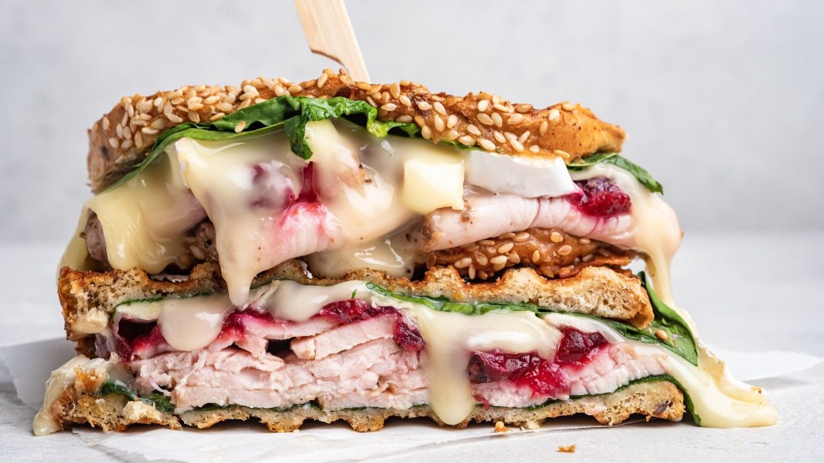 Saftiges Truthahn-Sandwich mit Cranberry-Sauce, Spinat, geschmolzenem Käse und Sesam auf einem weißen Teller