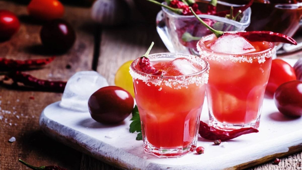 Zwei Gläser mit Chili-Kirsch-Mocktails stehen neben Kirschen und einer Schale voll Chilis