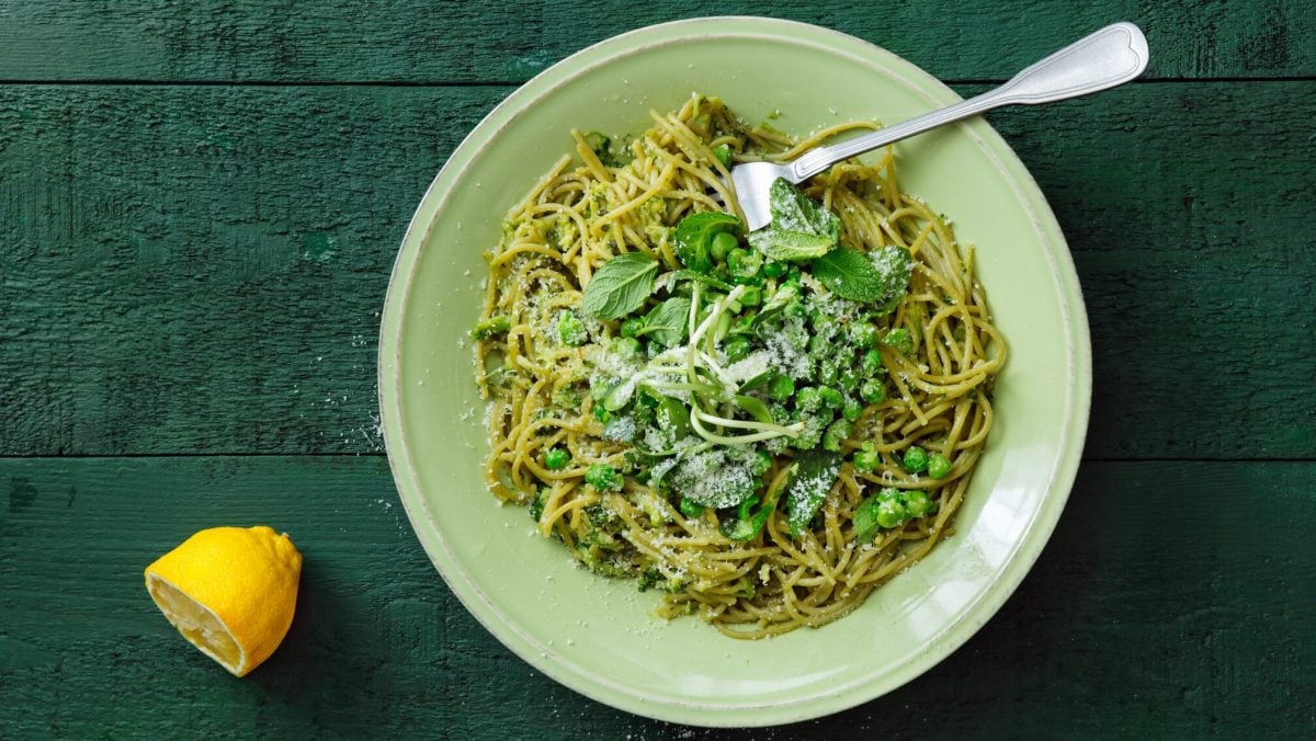 Frische Pasta-Bowl mit Erbsen und Minze auf weißem Teller vor grünem Untergrund