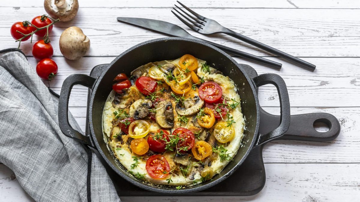 Würziges Omelette mit Tomate und Chili in schwarzer Pfanne vor hellem Untergrund