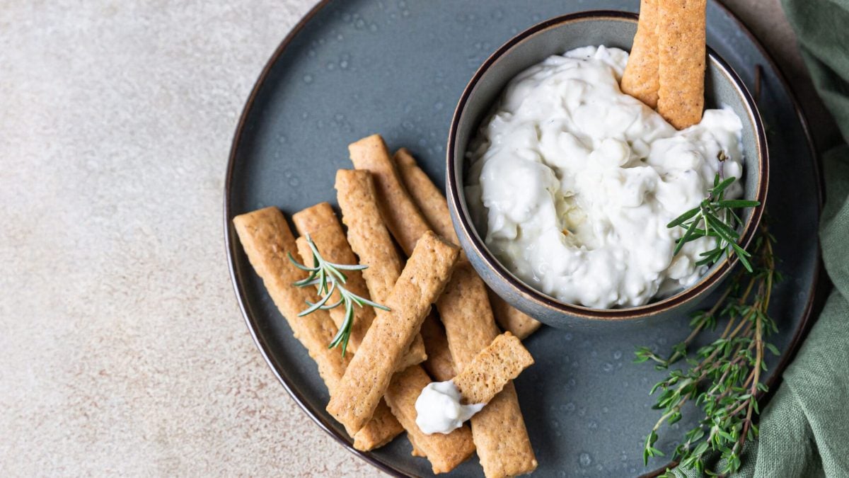 Schneller Birnen-Dip mit Gorgonzola in Schüssel auf blauem Teller, daneben Rosmarin und Brotsticks