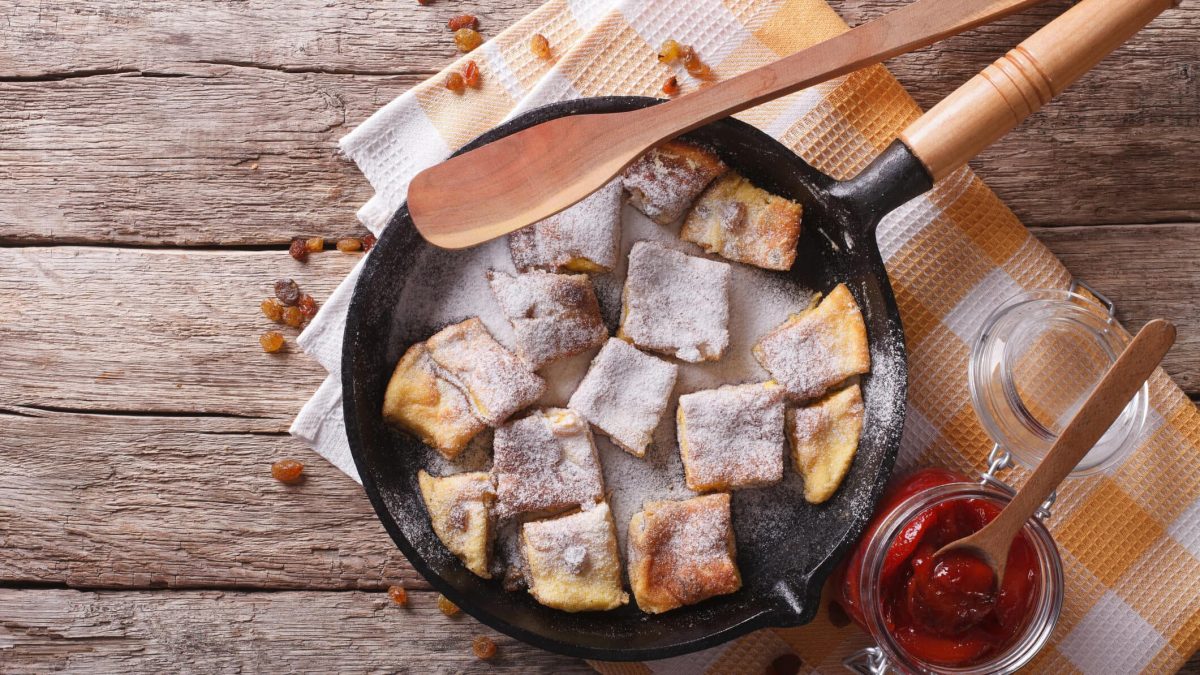 Kaiserschmarrn aus dem Ofen in Pfanne auf Holzuntergrund, daneben Zwetschgenkompott