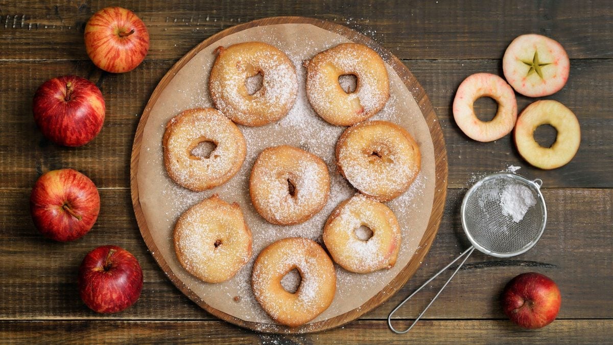 Selbst gemachte Apfelbeignets auf Teller, daneben Puderzucker