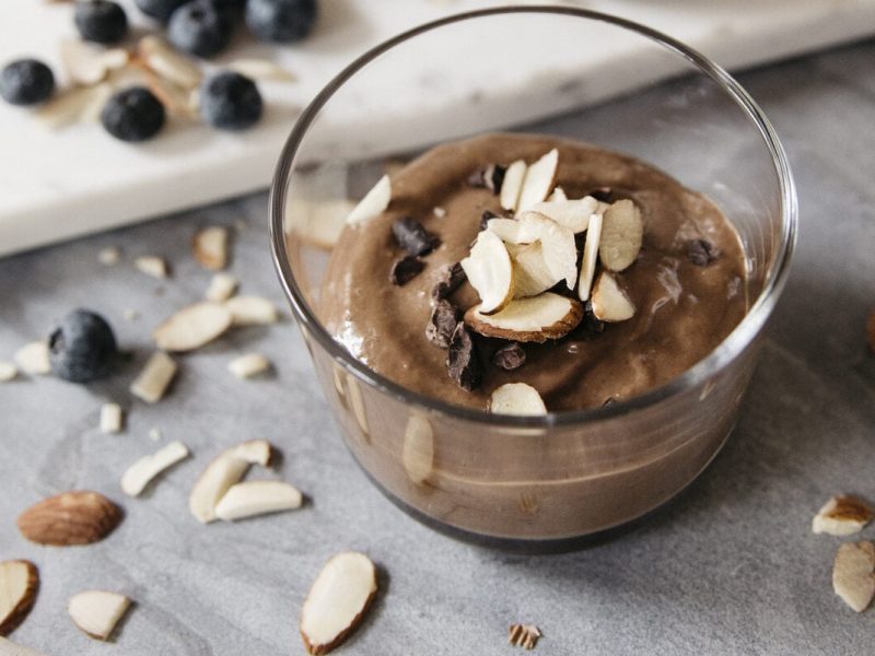 Schokoladiger Chia Pudding mit Mandeln in kleinem Glas, daneben Mandelsplitter