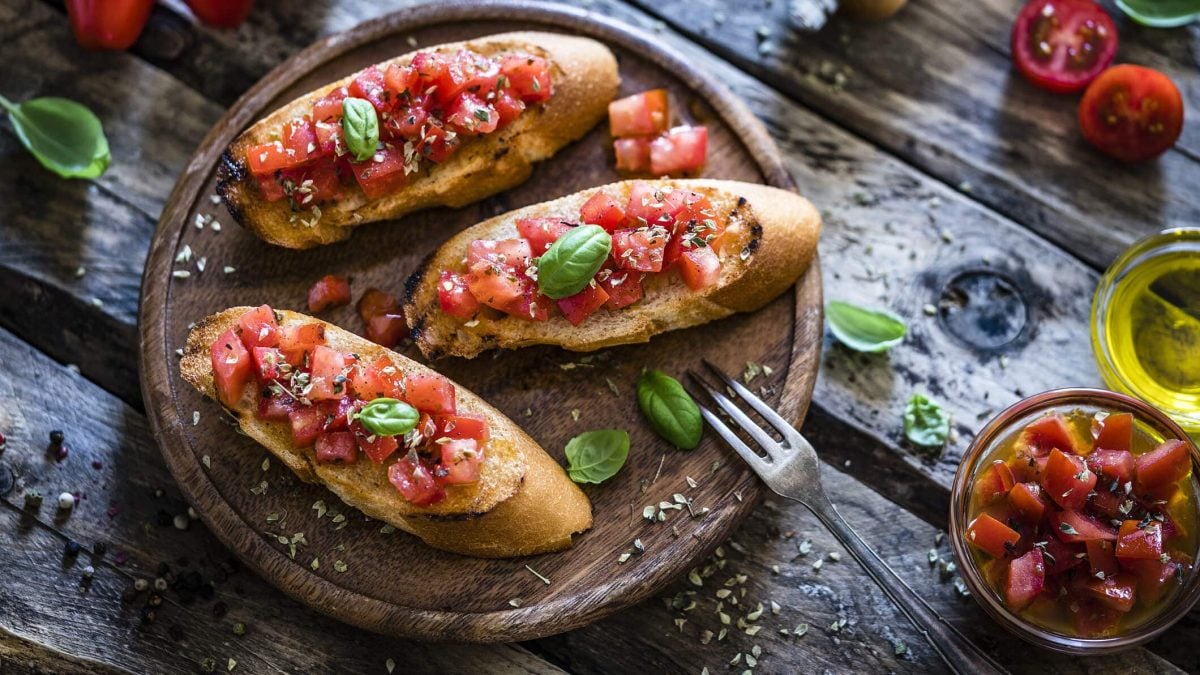 Einfache Tomaten-Bruschetta auf Holztablett, daneben Basilikum und Öl