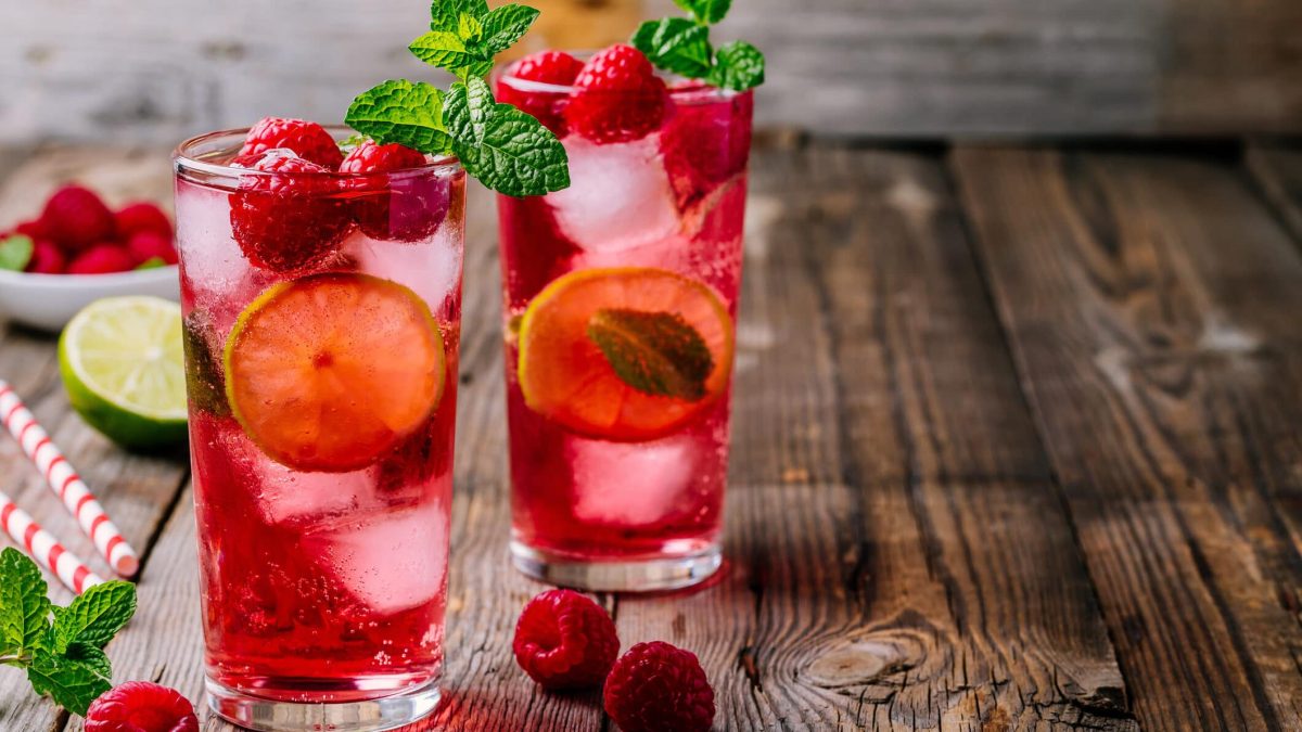 Selbst gemachter Himbeer-Eistee mit Minze auf Holzuntergrund, daneben Himbeeren