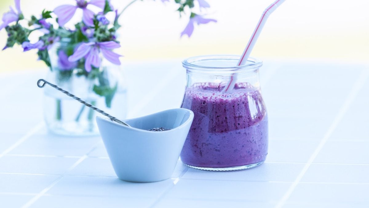 Brombeer-Smoothie mit Chia in hellem Ambiente neben lila Blüten.
