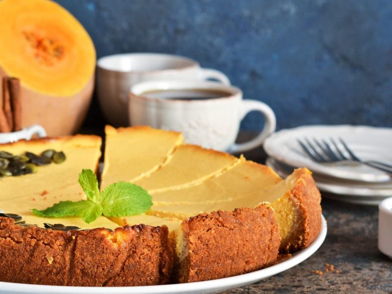 Cremiger Kürbis-Cheesecake auf weißem Teller garniert mit Kürbiskernen