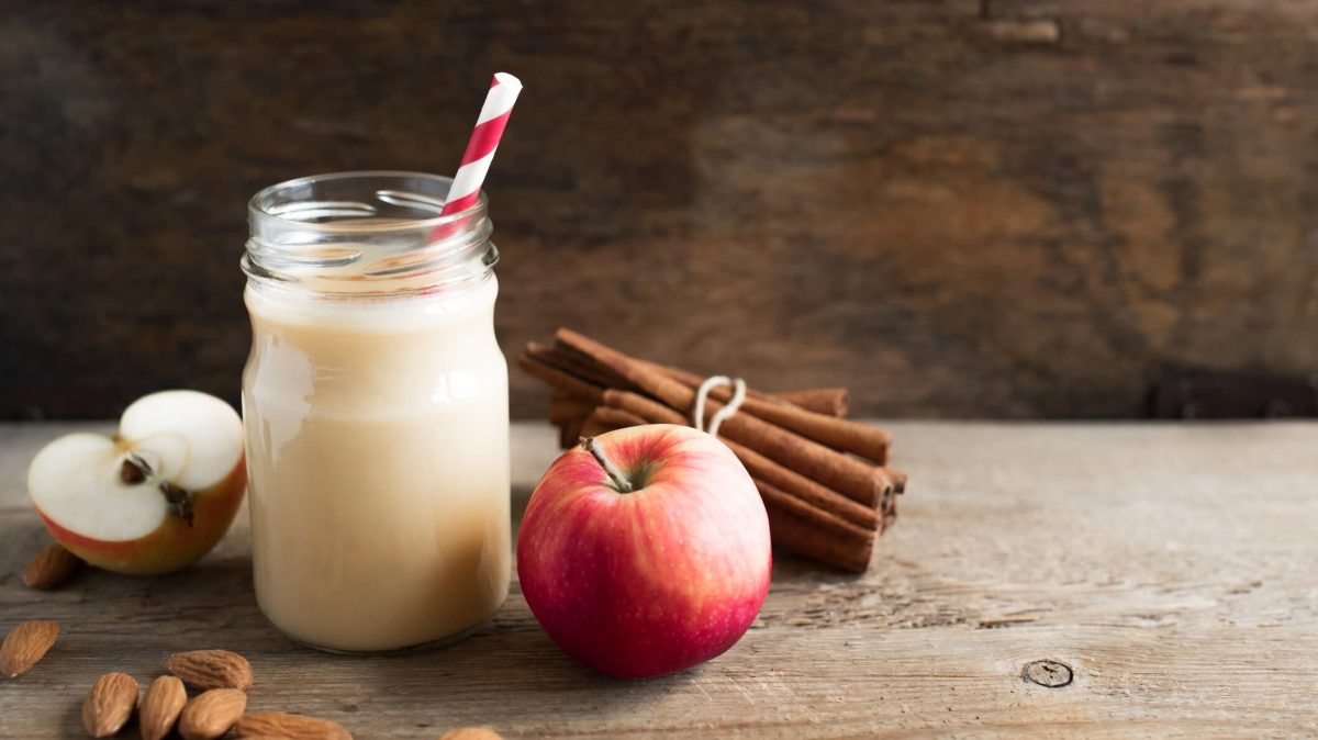 Power-Protein-Smoothie mit Apfel in Glas mit rotem Strohhalm, daneben Apfel und Zimtstangen