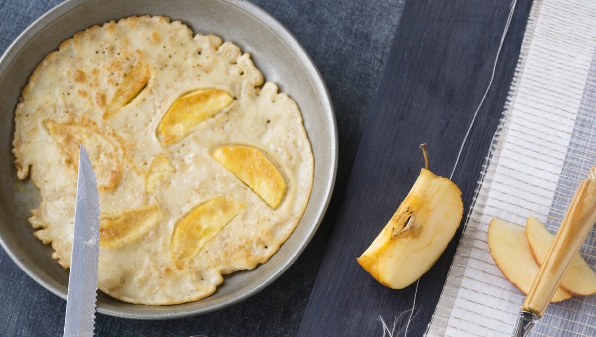 Schnelle Pfannkuchen mit Apfel in Pfanne, daneben Apfel
