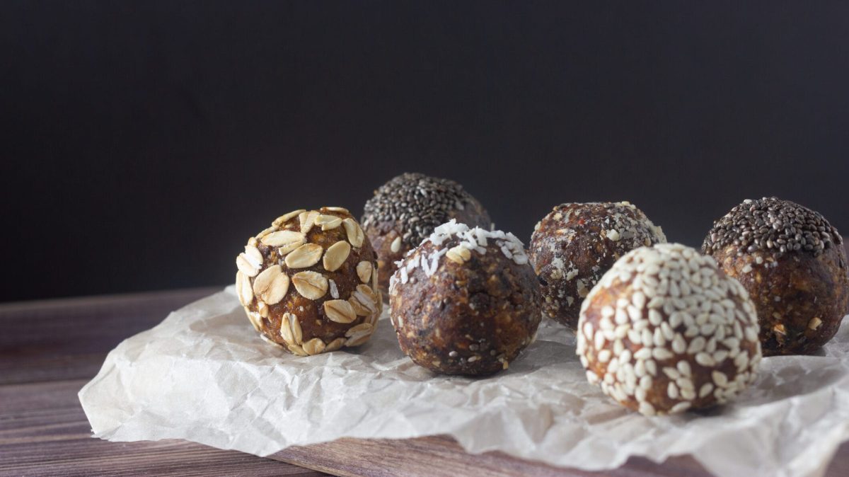 Schokoladige Energy-Balls aus Datteln auf Papierunterlage mit verschiedenen Garnituren