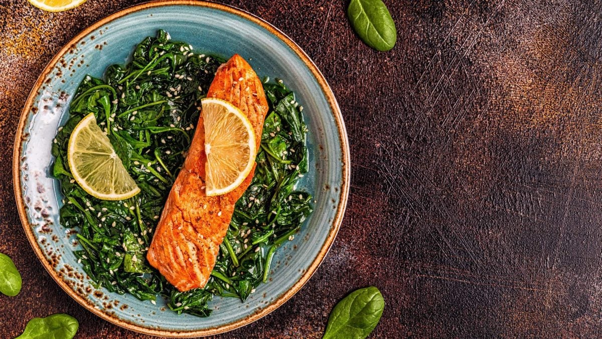 Asiatischer Lachs auf Spinatbett vor Holzuntergrund, garniert mit Limetten