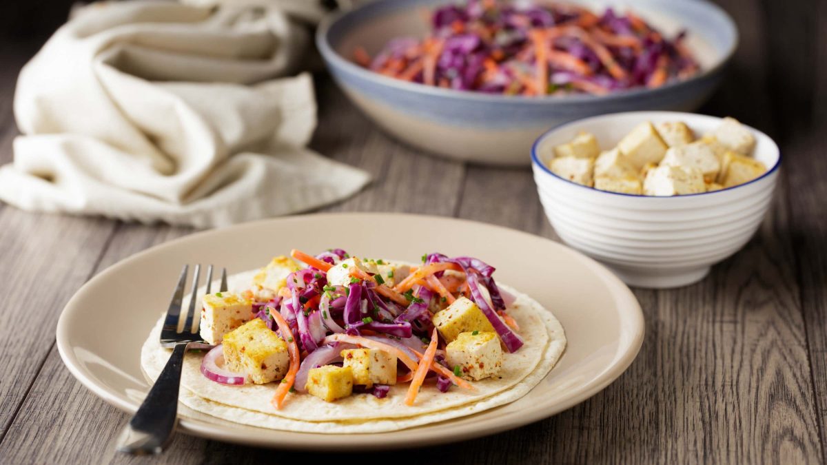 Tofu-Wrap mit Krautsalat auf einem hellen Teller, serviert mit frittierten Tofuwürfeln und Krautsalat in verschiedenen Schalen auf einem Holztisch
