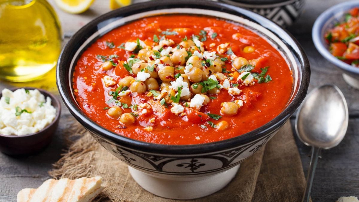 Tomatensuppe mit Quinoa und Hüttenkäe in schwarz-weißer Schüssel auf Holzuntergrund