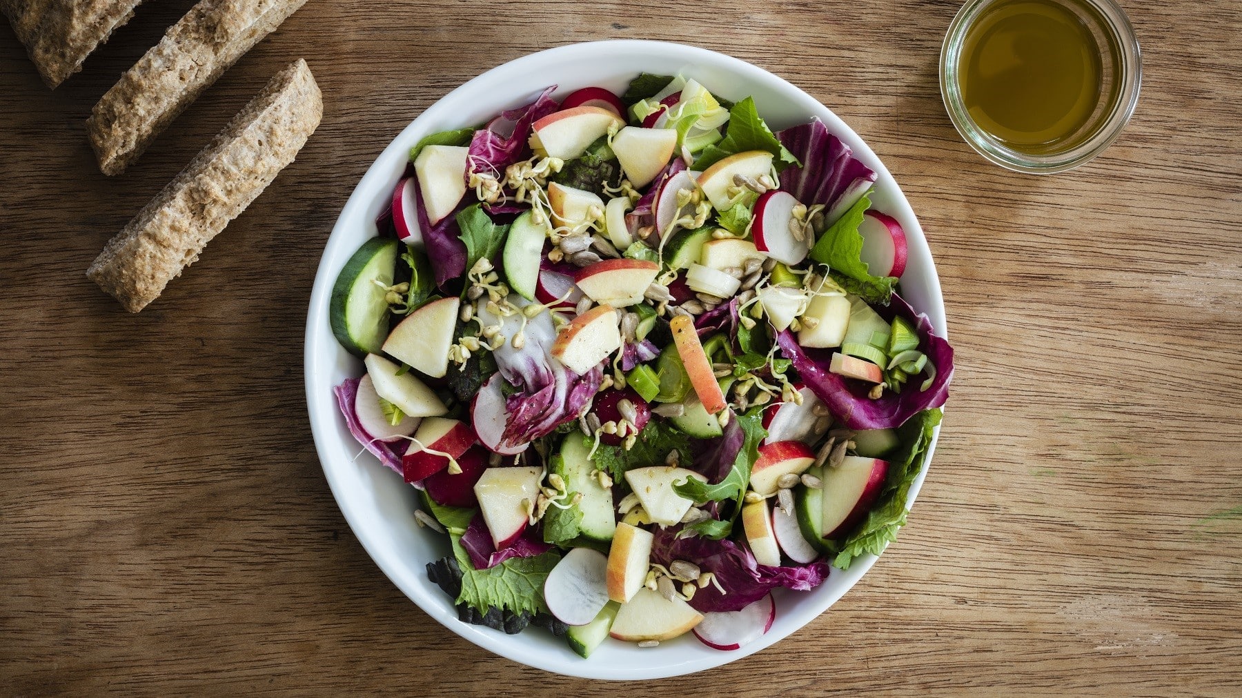 Bunter Apfelsalat mit Radicchio, Gurke, Roma-Salat, Sprossen und leichter Salat-Sauce, serviert in einer großen Schale auf einem Holztisch mit Brot.