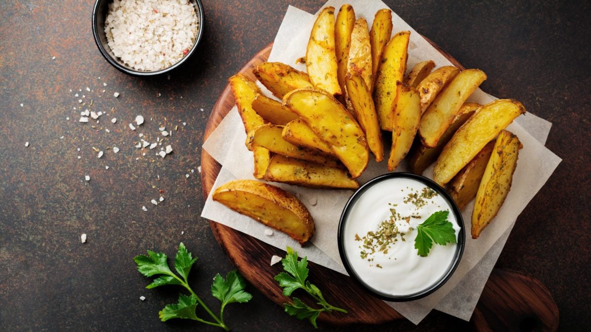 Kartoffel Wedges mit Skyr-Dip auf Papier, daneben Petersilie vor schwarzem Untergrund