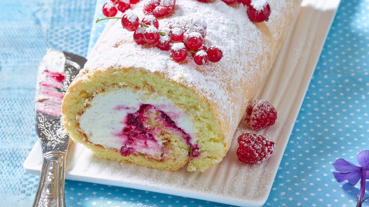 Biskuitrolle mit Roter Grütze auf blauem Untergrund
