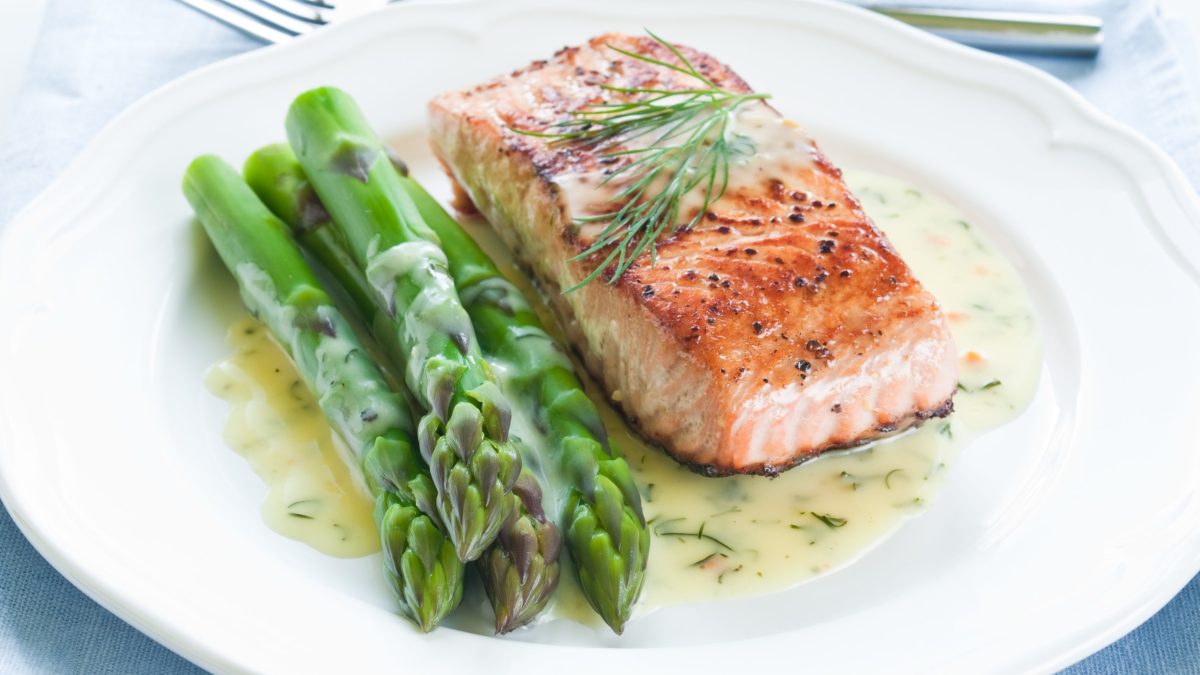 Selbst gemachte Honig-Dill-Senfsauce mit Ofenlachs und grünem Spargel auf weißem Teller und hellem Untergrund. Draufsicht.