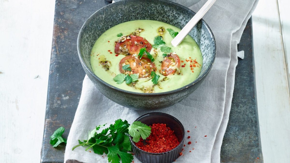 Kalte Avocado-Suppe mit getrockneten Tomaten in grauer Schüssel, daneben Chilliflocken