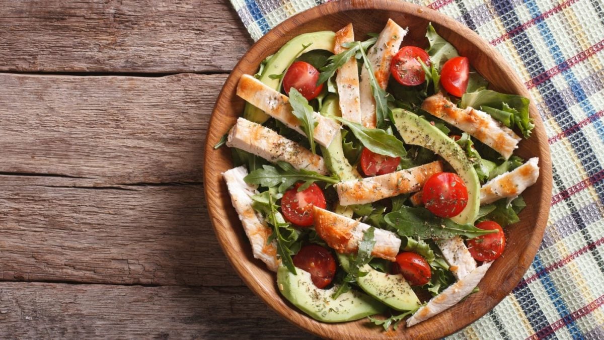 Draufsicht: Avocadostreifen, Hähnchenstreifen, halbierte Kirschtomaten, Rucolablätter.