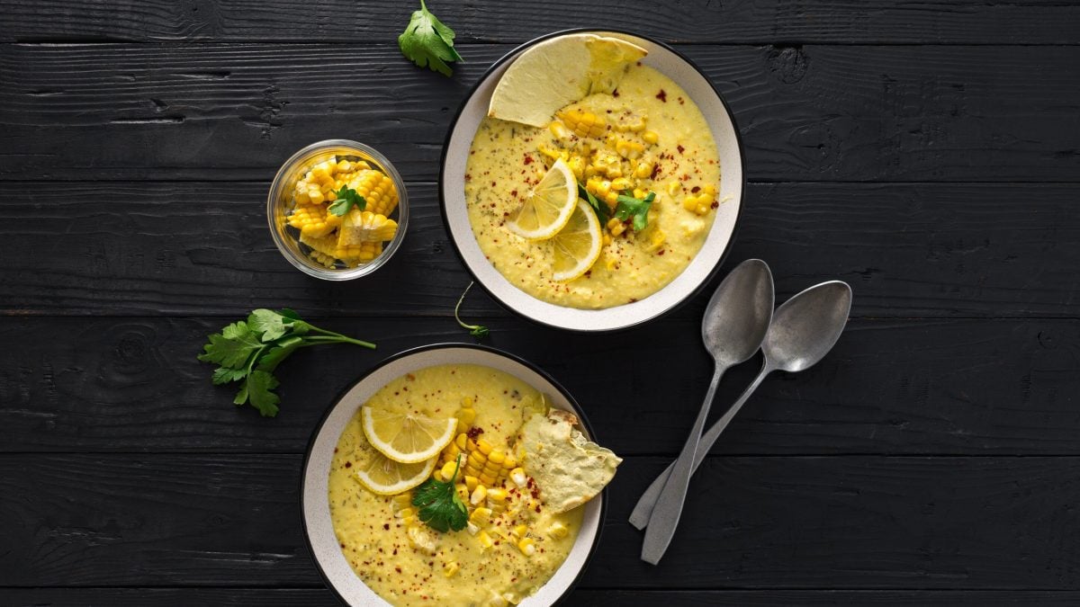 Zwei Teller mit cremiger Maissuppe mexikanischer Art gespickt mit Zitronenscheiben und Korianderblättern auf schwarzem Hintergrund
