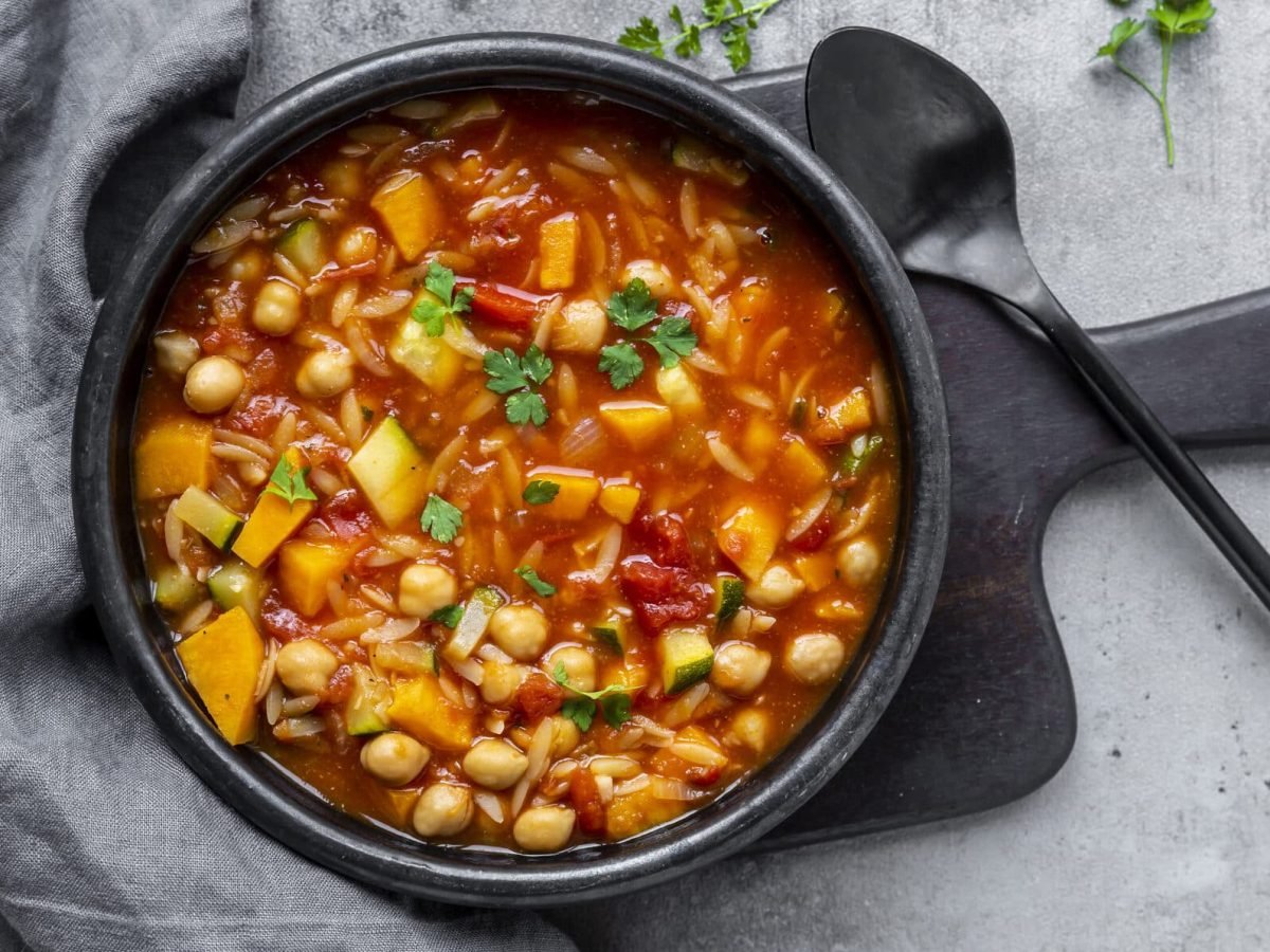 Leichter Kichererbsen-Eintopf mit Zucchini in Pfanne auf schwarzem Brett