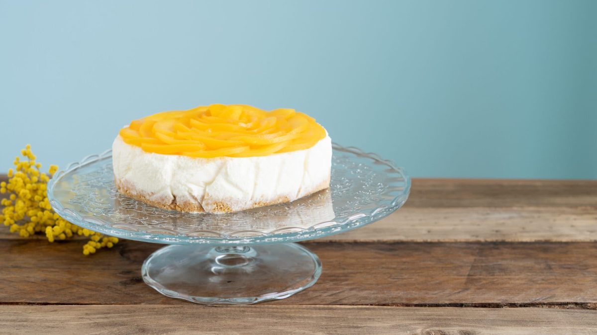 Ausgefallene Sekttorte mit Aprikosen auf Kuchenplatte vor blauer Wand