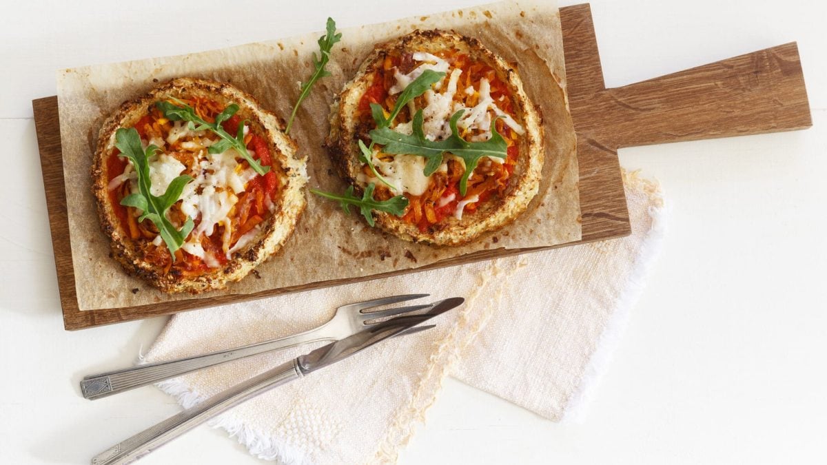 Protein-Pizza aus Blumenkohl auf Holzbrett garniert mit Rucola