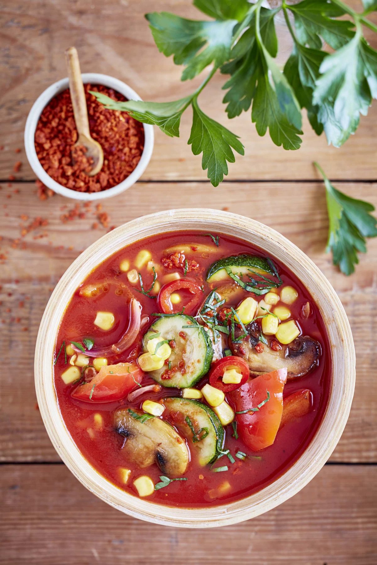 pikante Gemüsesuppe mit Chili und Mais in Schüssel, daneben Chilli und Petersilie