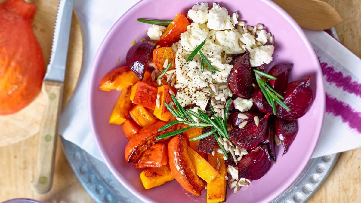 Herbstliche Buddha-Bowl mit Feta-Topping in pinker Schüssel, daneben Messer
