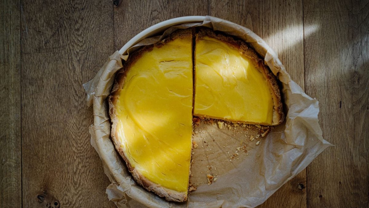 angeschnittene Tarte au Citron in Backpapier und Backform auf holzigem Untergrund