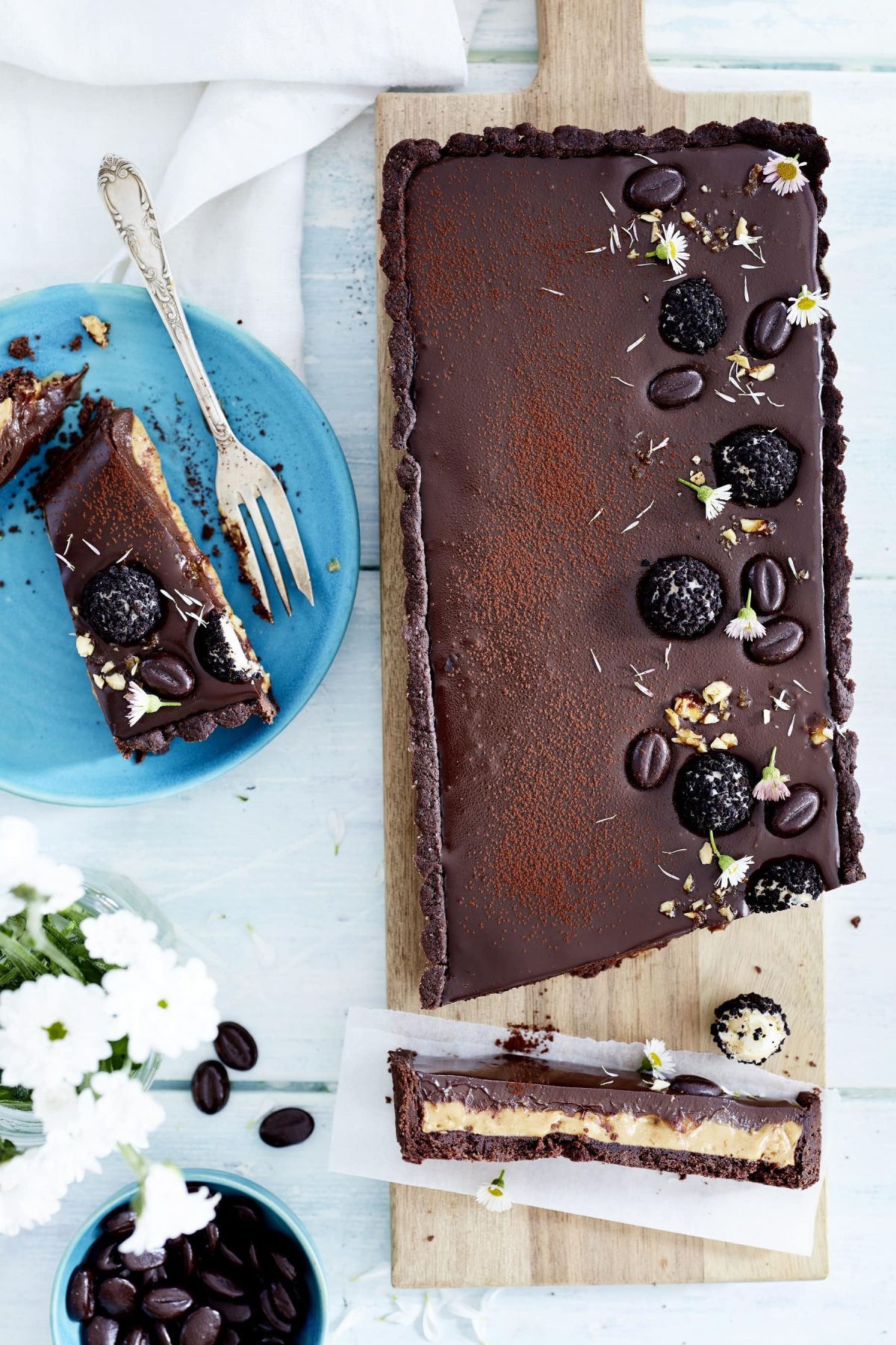 Tarte au Chocolat mit Erdnuss und Espresso auf Holzbrett, ein Stück auf blauem Teller