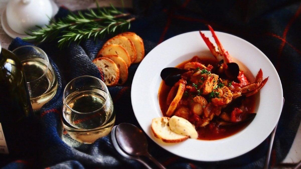 Weißer Teller mit Bouillabaisse, zwei Gläsern Weißwein und Weißbrot