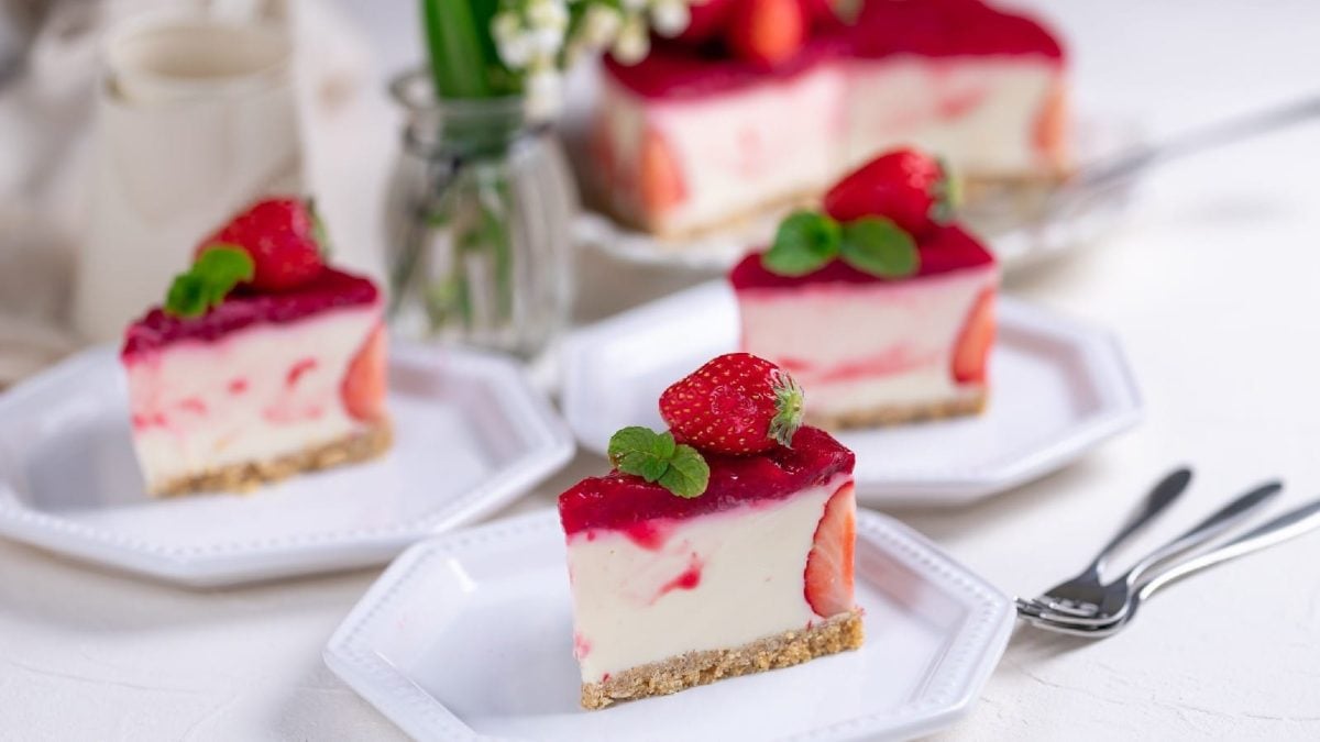 Beeren-Quark-Torte auf Tellern mit Besteck auf einem gedeckten Tisch mit Blumen in einer Vase