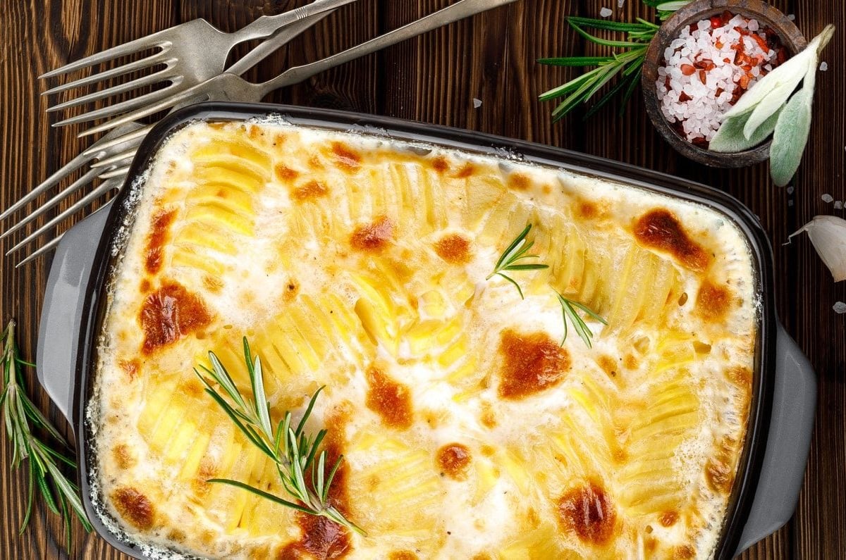 Draufsicht: Eine Auflaufform mit einem Gratin auf einem dunklen Untergrund aus Holz.