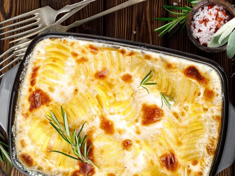 Draufsicht: Eine Auflaufform mit einem Gratin auf einem dunklen Untergrund aus Holz.