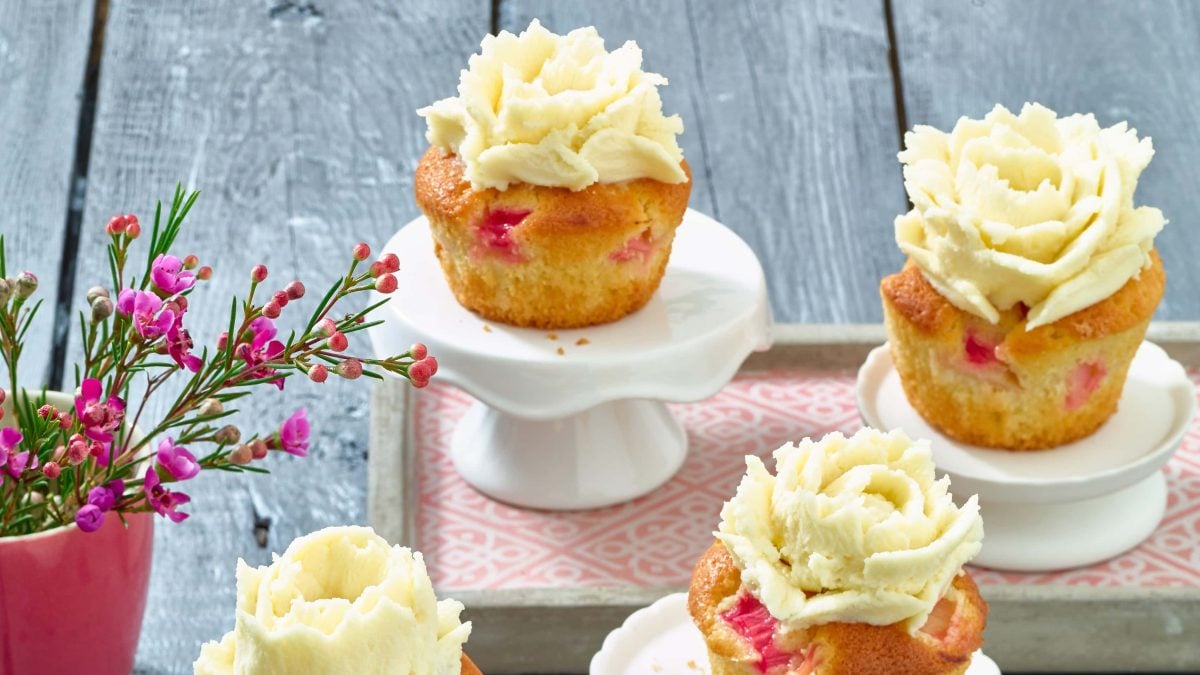Rhabarber-Cupcakes mit Marzipan stehen auf kleinen Etageren neben einer Vase mit Blumen