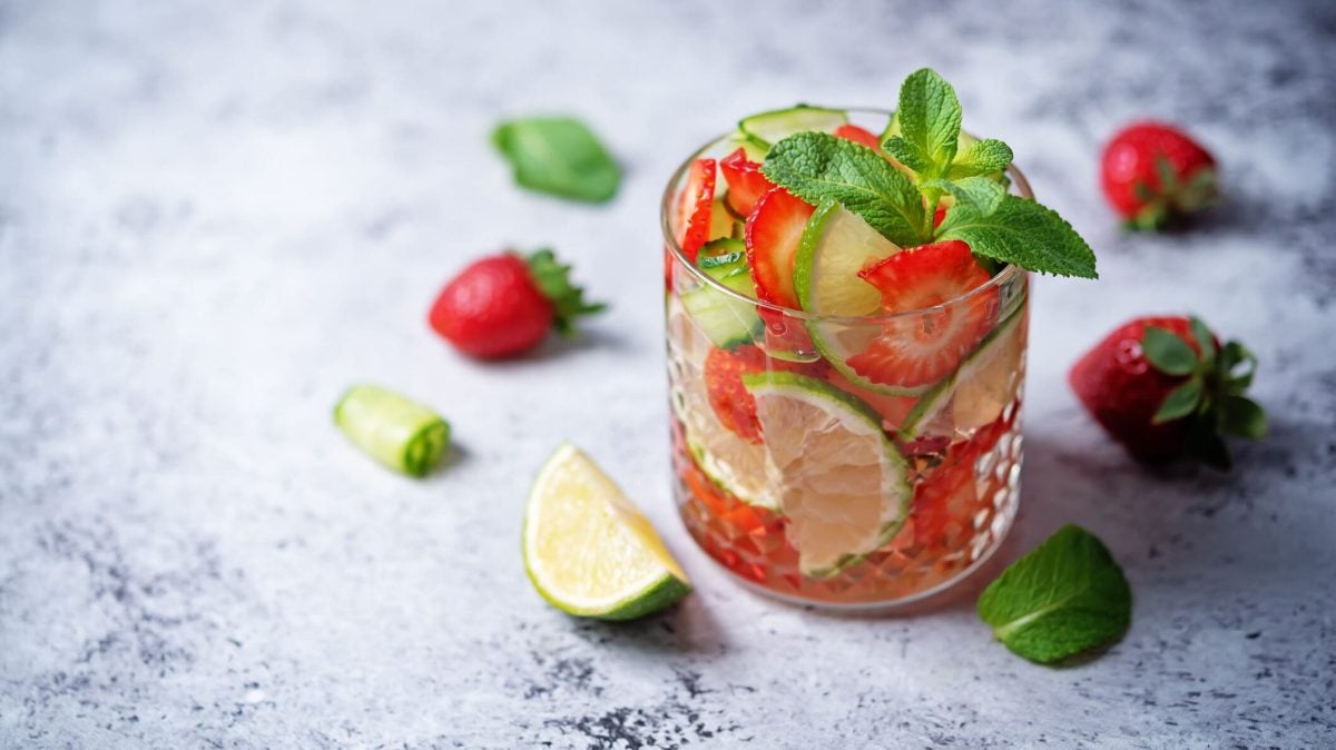 Alkoholfreier Caipirinha mit Erdbeere und Basilikum, daneben geschnittene Limetten
