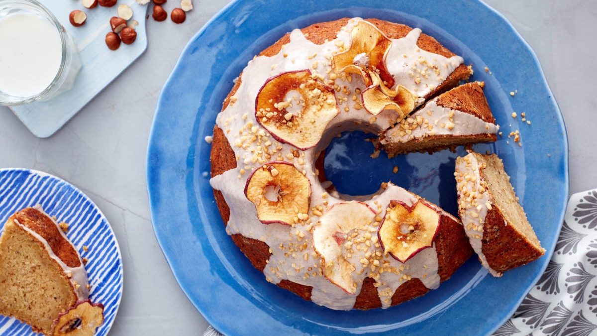 Ein mit Äpfeln bedeckter Apfel-Nuss-Gugelhupf auf einem blauen Teller drapiert