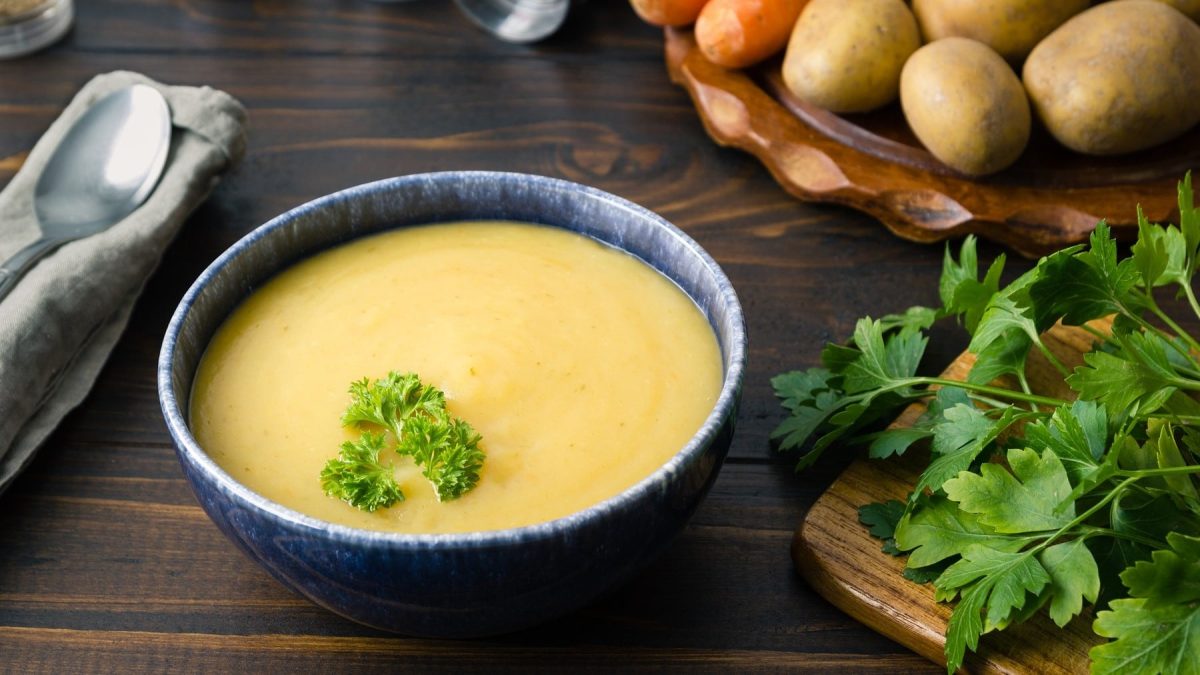 Pürierte Kartoffel-Cremesuppe mit Wurzelgemüse und garniert mit frischer Petersilie in einer dunklen Schale auf einem rustikalen Tisch.