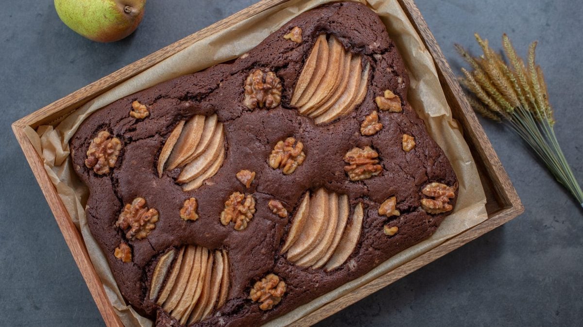 Schoko-Birnenkuchen mit Walnüssen in Backform, daneben getrocknete Gräser