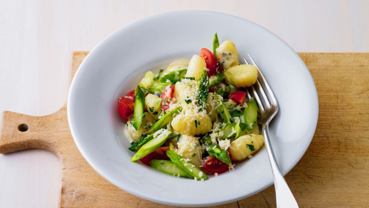 Ein weißer Telle mit Gnocchi mit grünem Spargel, Tomaten und Käse
