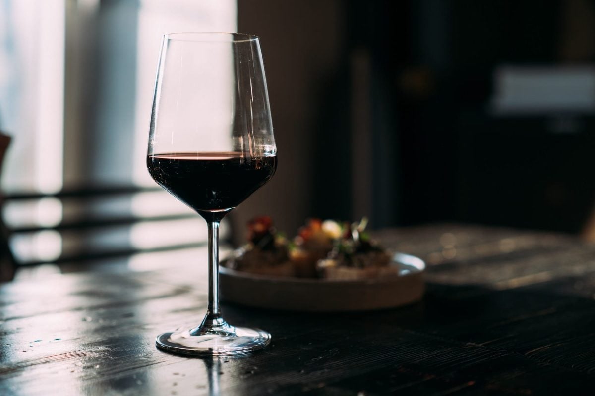 Ein Glas Rotwein auf einem dunklen Holztisch vor einem dunklen Hintergrund.